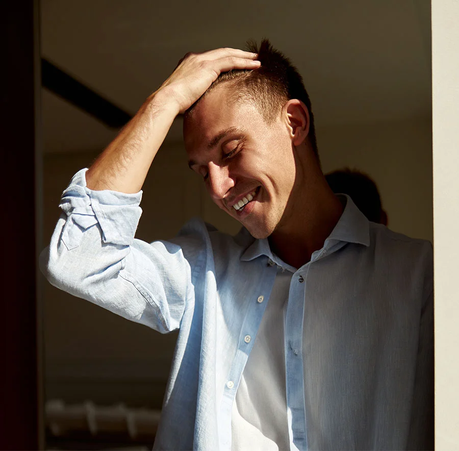 A blonde man smiling with eyes close, as the sun falls on his face, hand in his hair - Ear Surgery in Chicago, IL