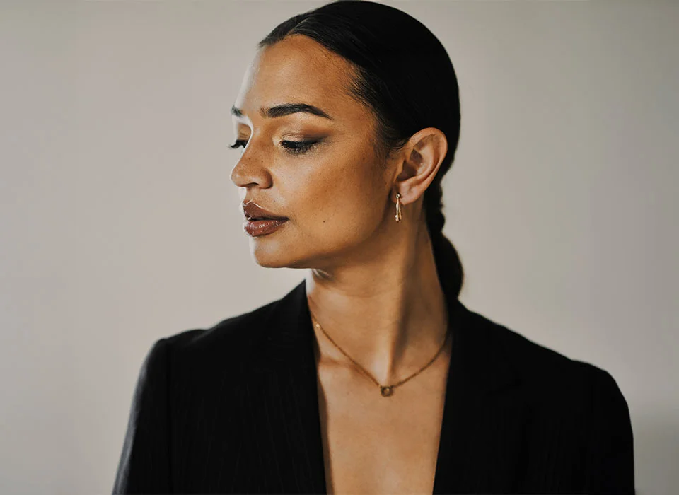 A woman with her dark hair in a braid, wearing a black blazer, wearing gold jewelry, looking to the side - Ear Surgery in Chicago, IL