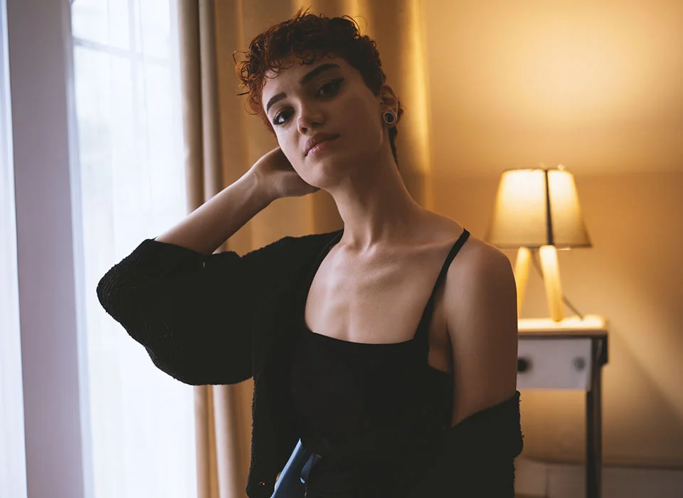 A woman in front of yellow curtains, wearing a black top and cardigan, with a stretched ear piercing - Earlobe Repair Procedure in Chicago, IL