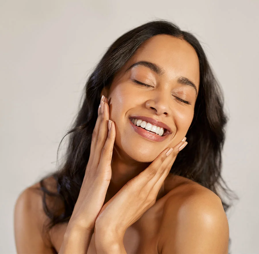 A woman with long black hair, smiling with her eyes closed and face rested in her hands - Fat Transfer Procedure in Chicago, IL